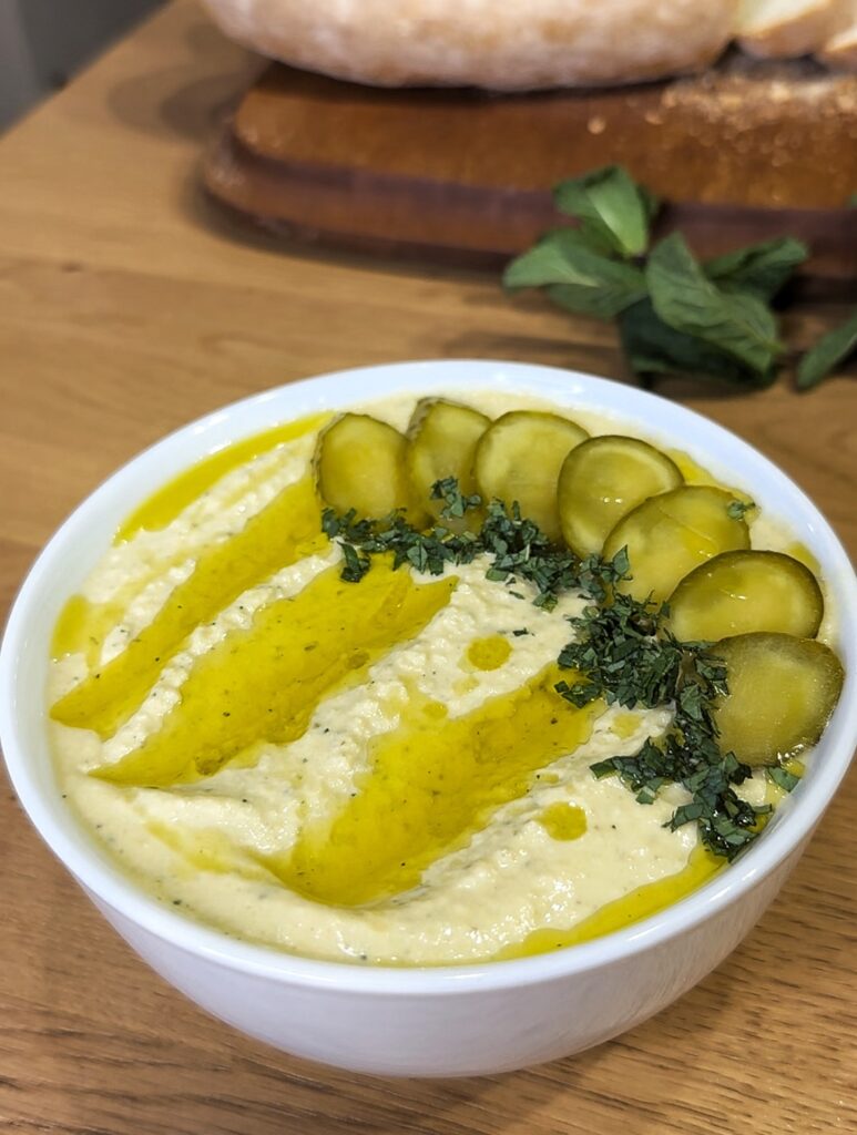 Ciotola di humus di ceci ai cetriolini sottaceto, decorata con cetriolini, olio d'oliva e menta tritata